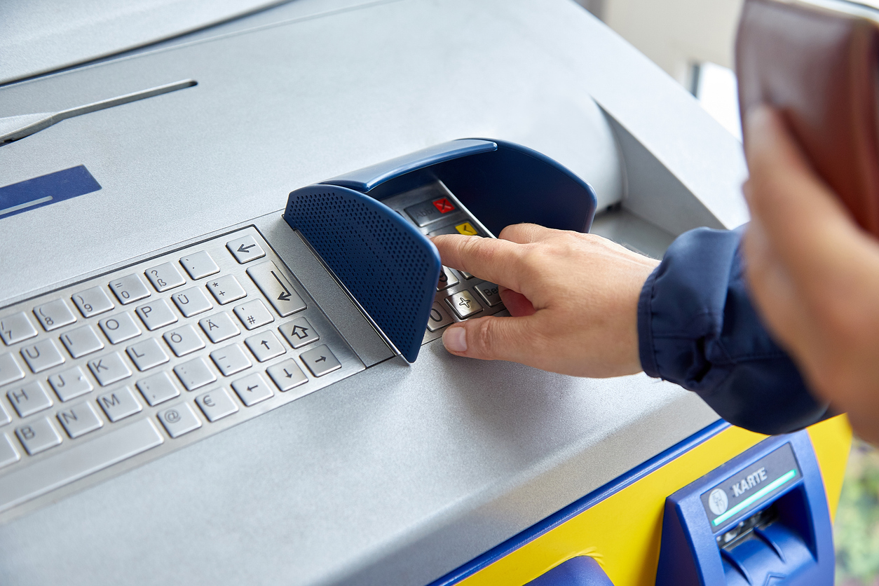 A female hand dials a personal code on the ATM keyboard openly.