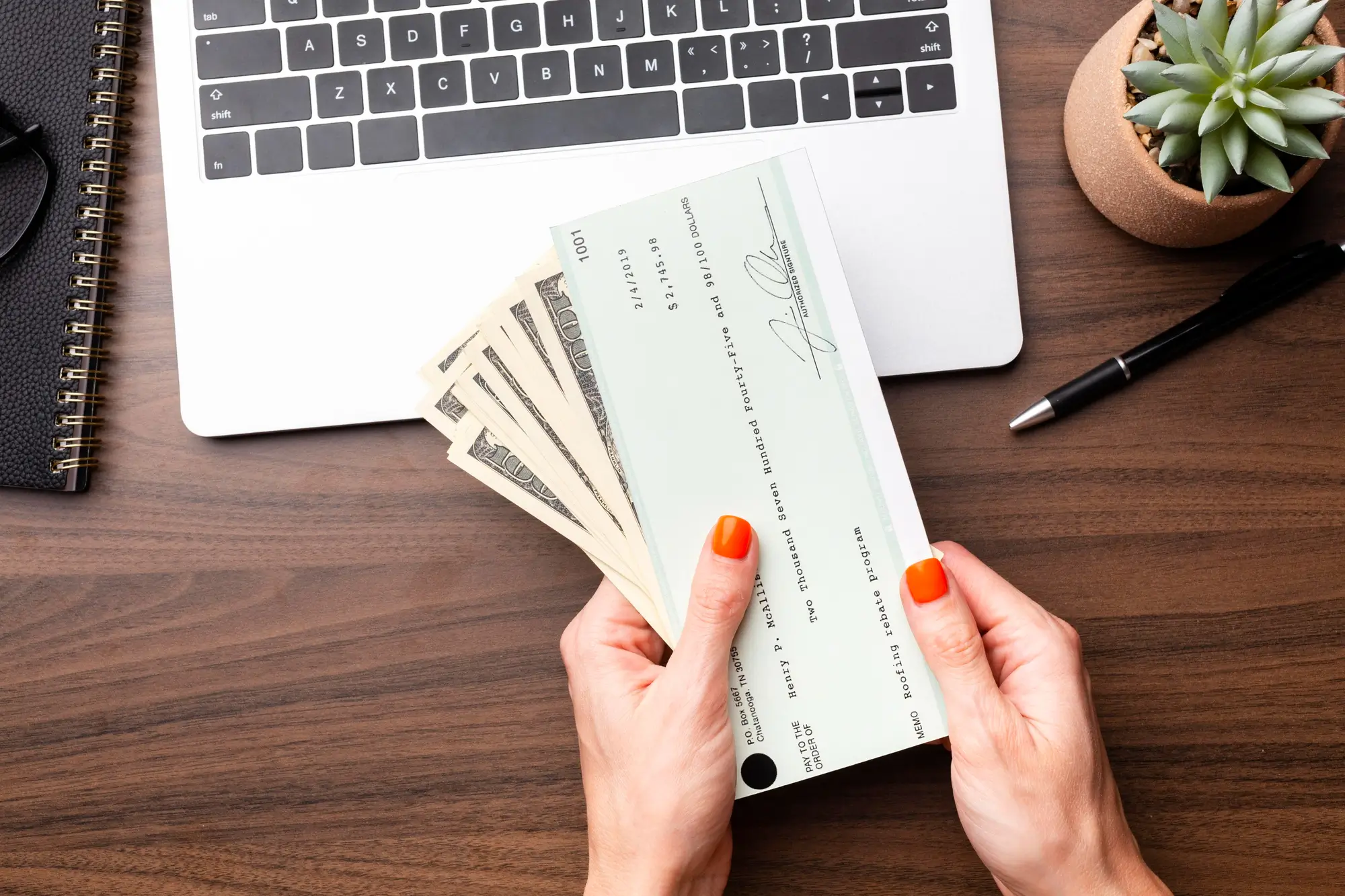 Hands organizing a check and cash in front of laptop