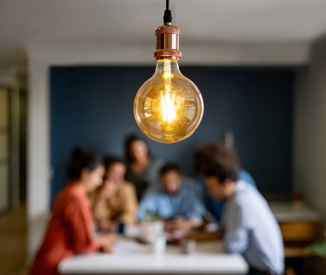 People sitting around a table with a bright light bulb hanging above them
