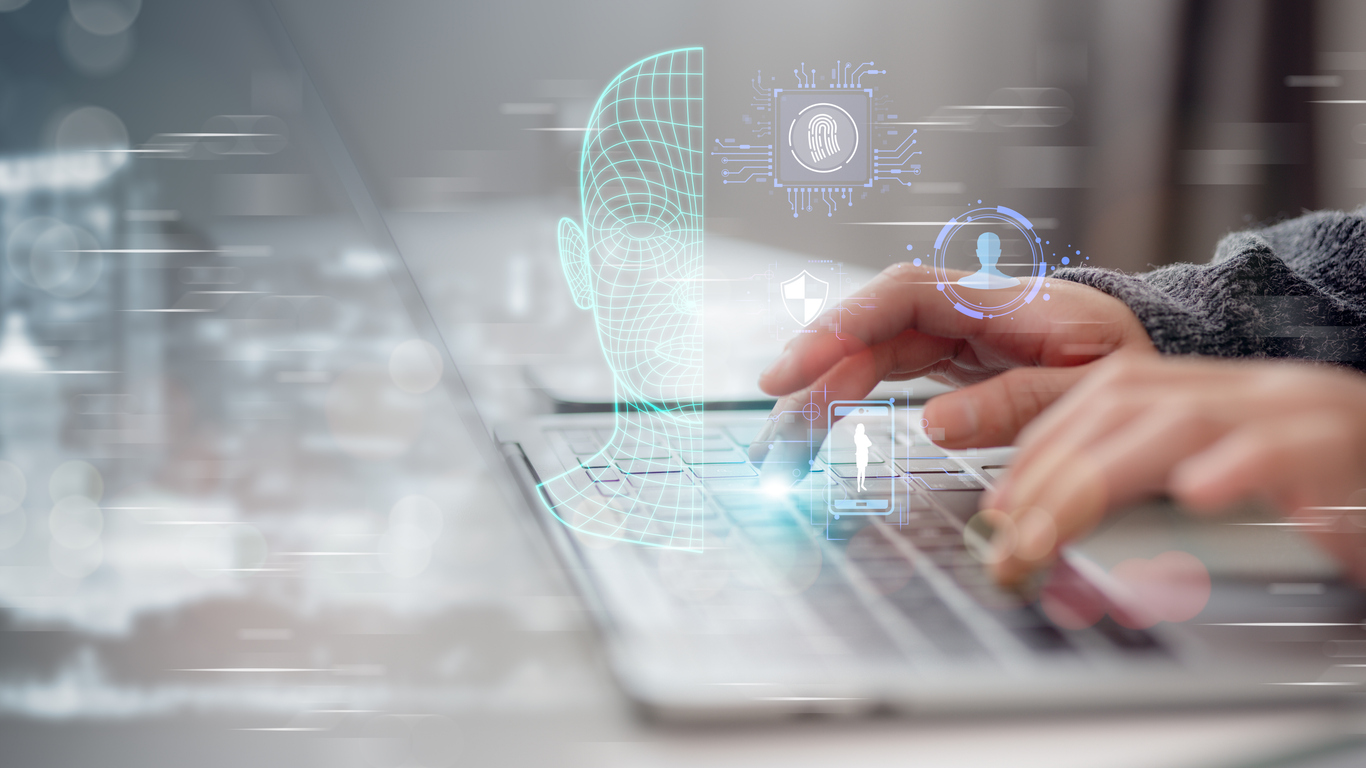 Hands typing on laptop with floating fingerprint and facial recognition software graphics above.