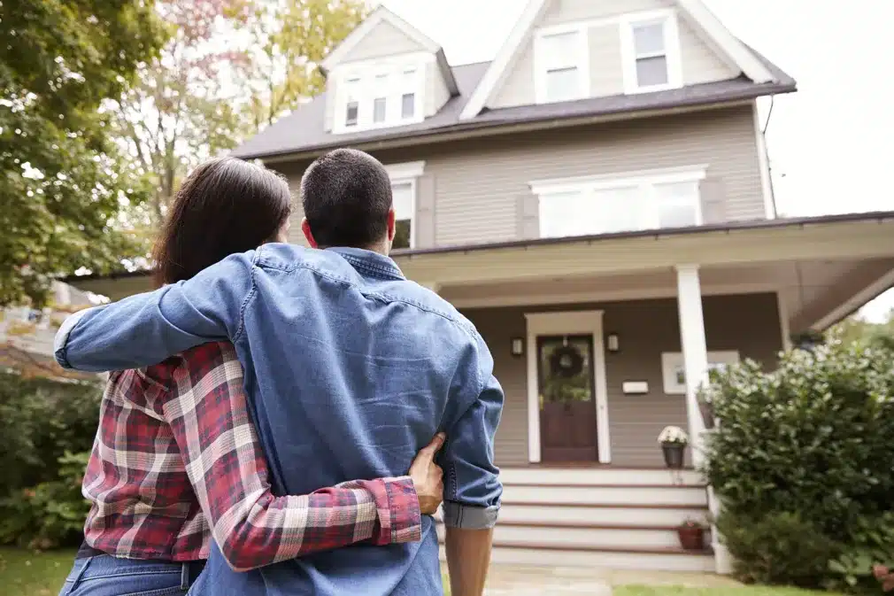 Couple with their arms around each other, standing in front of a house